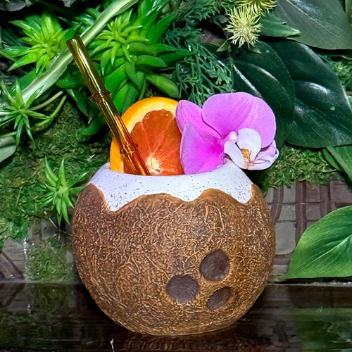 The Kokomo Coconut Ceramic Tiki Mug, available for a limited-time pre-order, features a tropical drink presentation with a gold straw and garnishes of orange slice and pink orchid, set against lush green foliage. Its an exotic delight worth anticipating.