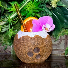 The Kokomo Coconut Ceramic Tiki Mug, featuring a tropical drink with a pink orchid and orange slice garnish, white rim, and gold straw against lush green leaves, is available in limited quantity. Dont miss out on this limited-time pre-order!.