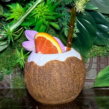 Sip your drink from the Kokomo Coconut - Ceramic Tiki Mug, featuring a cracked shell design, pink flower garnish, and orange slice. Complete with a bamboo straw, this limited-time pre-order offers an exclusive experience amidst lush green foliage for those seeking unique creations.