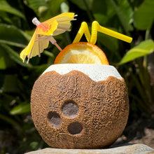 Pre-order the Kokomo Coconut, a limited edition ceramic tiki mug featuring a coconut shape, yellow umbrella, straw, and orange slice. It evokes a tropical vibe against green leaves. Secure yours for the next shipment now!.