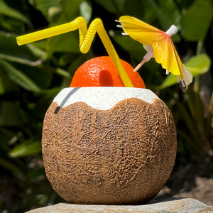 Savor a tropical drink in the Kokomo Coconut ceramic tiki mug, complete with a yellow umbrella and twisted straw, topped by an orange sphere. Nestled amidst lush green foliage, its the perfect exotic delight. Pre-order this limited-time offer today!.